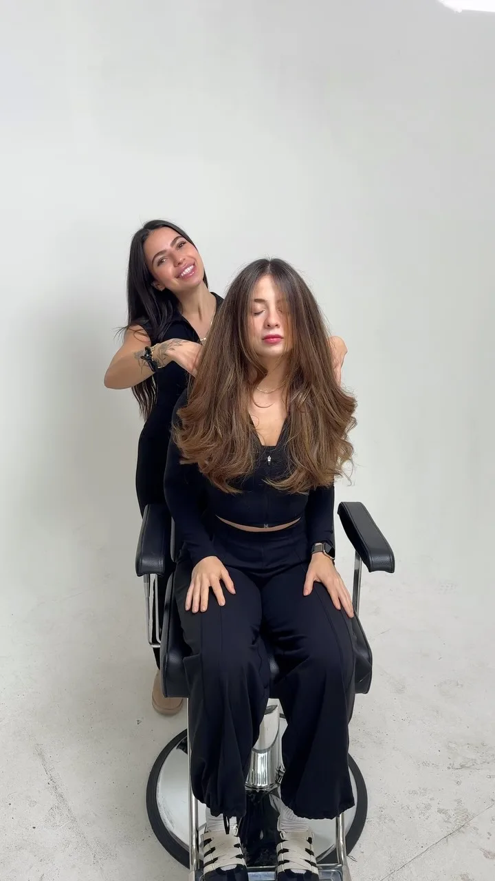 A client in the chair with her finished, glossy waves, her stylist just behind